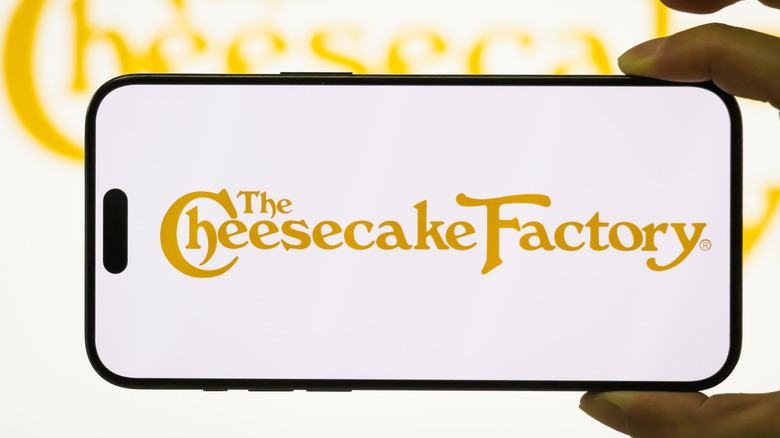 Person holding phone with The Cheesecake Factory sign