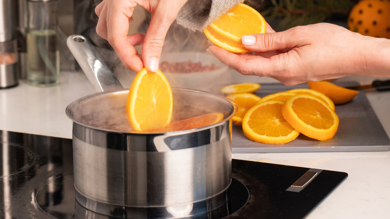Person putting orange slices into pot of simmering mulled wine
