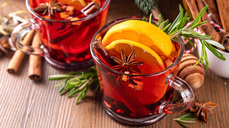 Mugs of mulled wine filled with spices, citrus, and herbs
