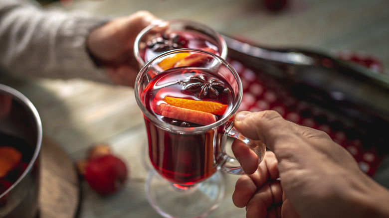 Hands holding mugs of mulled wine with citrus