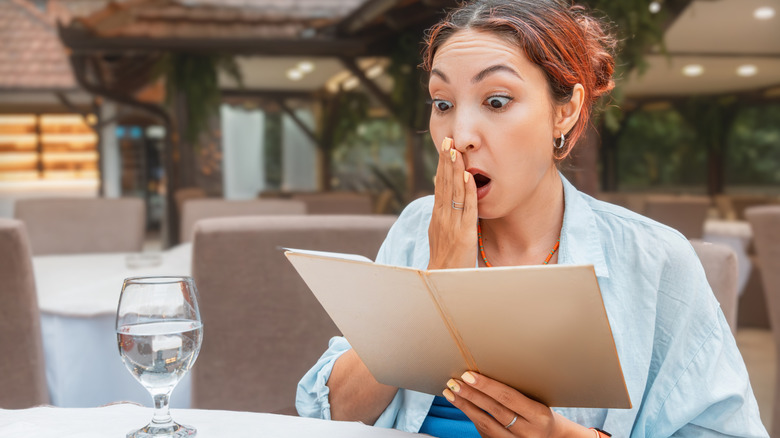 A woman looking surprised and shocked while holding a menu