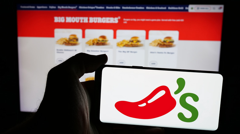 Hand holding a phone with Chili's logo against a Chili's menu on a computer
