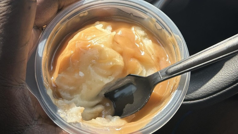 Hand holding KFC mashed potatoes and gravy in car