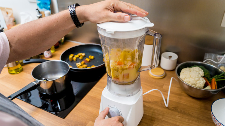 Hands using white blender on wooden countertop