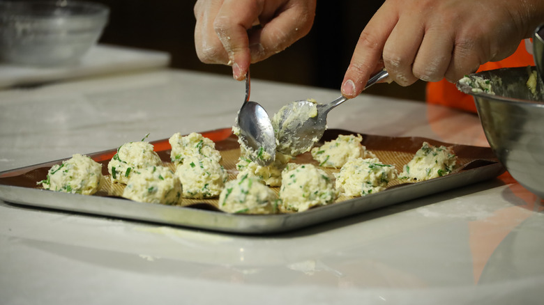 person dropping biscuits onto a baking sheet