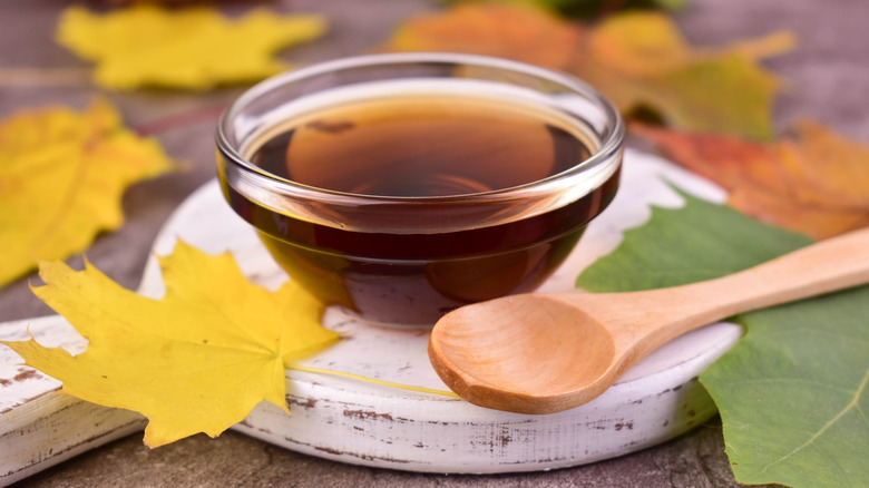 Maple syrup in small glass bowl with wooden spoon and leaf