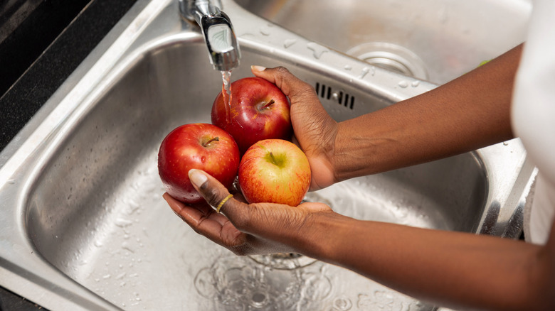 Hands washing apples over sink