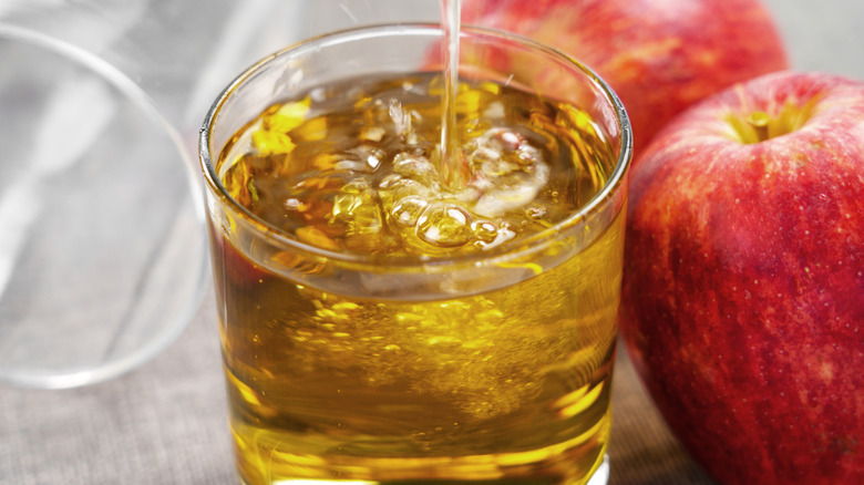 Cold apple cider in glass in front of red apples