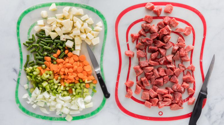 A green cutting board with fresh produce next to a red cutting board with raw meat