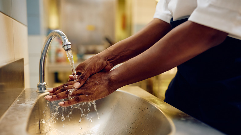 A food service worker washing their hands in a handwashing sink