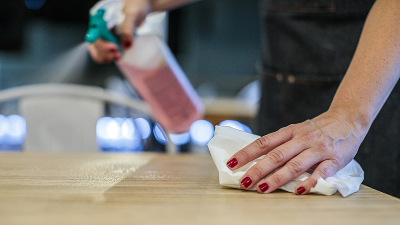 A food service worker spraying and wiping a table