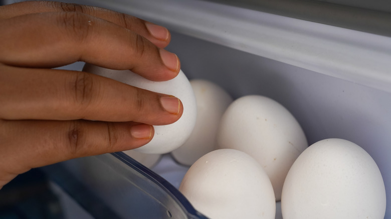 A person taking an egg out of a refrigerator