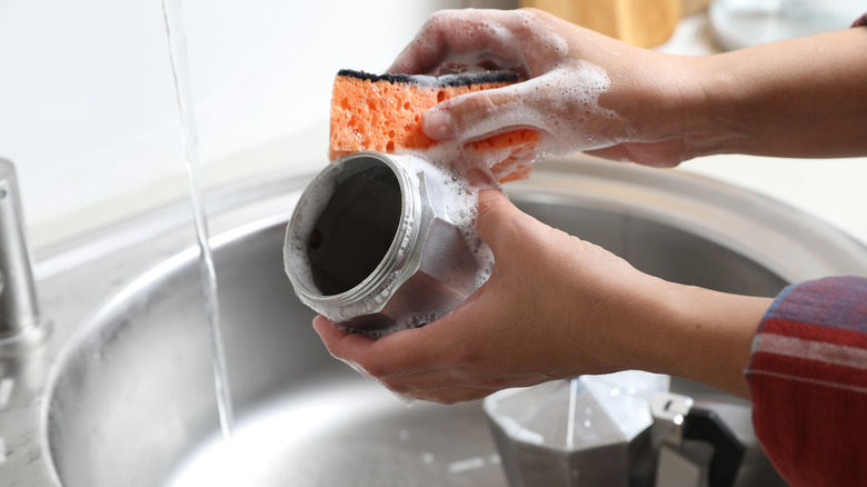 Someone washes Moka pot with soap and a sponge.