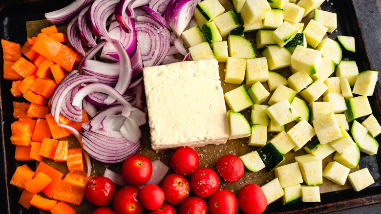 Block of feta cheese and diced carrots, zucchini, tomatoes, and onions on a baking sheet