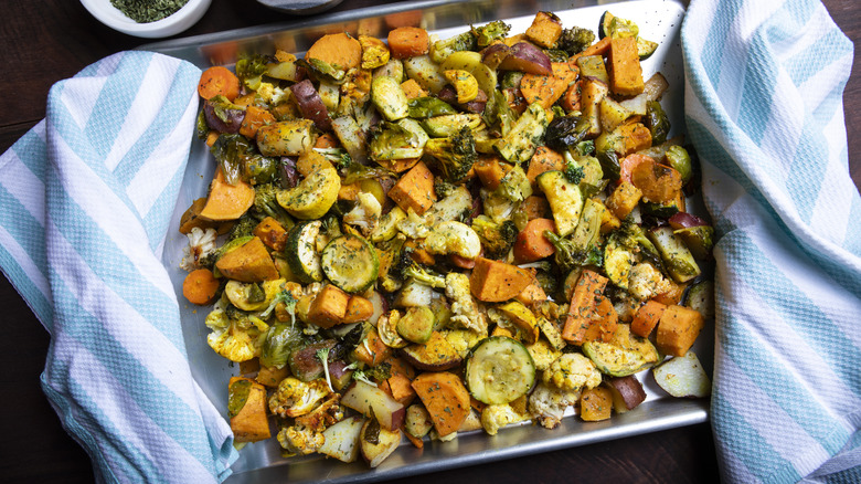 Roasted vegetables inside a sheet pan with kitchen towels on the sides