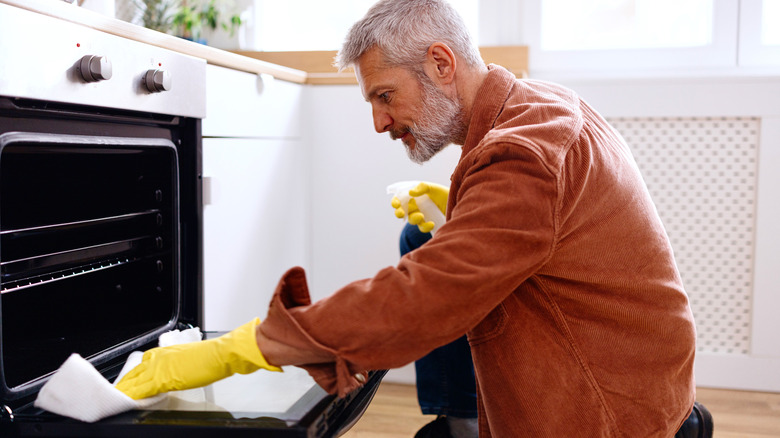 Person cleaning oven door with spray and cloth