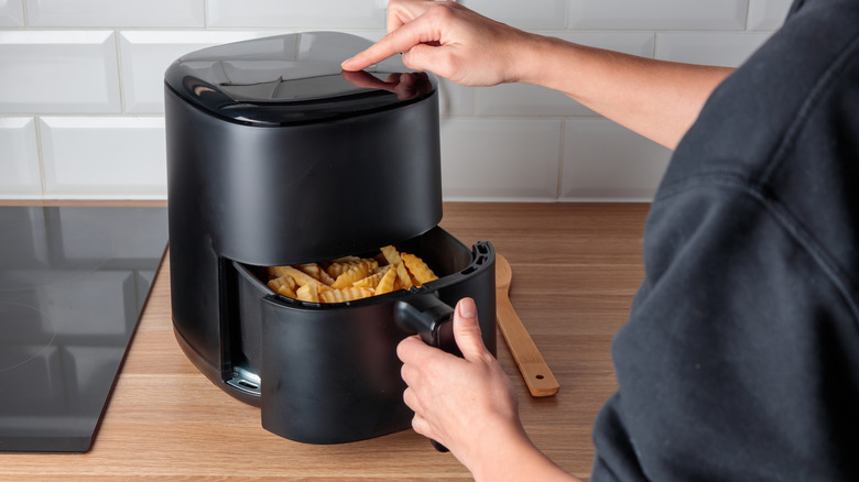Person opening air fryer drawer with crinkle fries inside