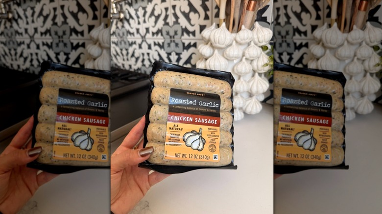 Hand holding package of Trader Joe's Roasted Garlic Chicken Sausage in kitchen