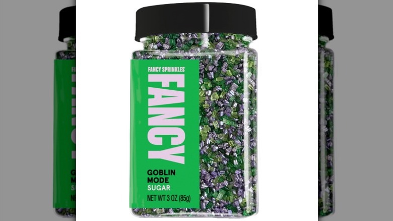 A bottle of Fancy Sprinkles sugar sprinkles with green, purple and black crystals on white background