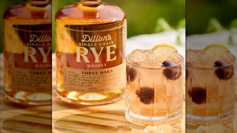Bottle of Dillon's Whisky next to glass of cocktail with cherries on a cutting board.