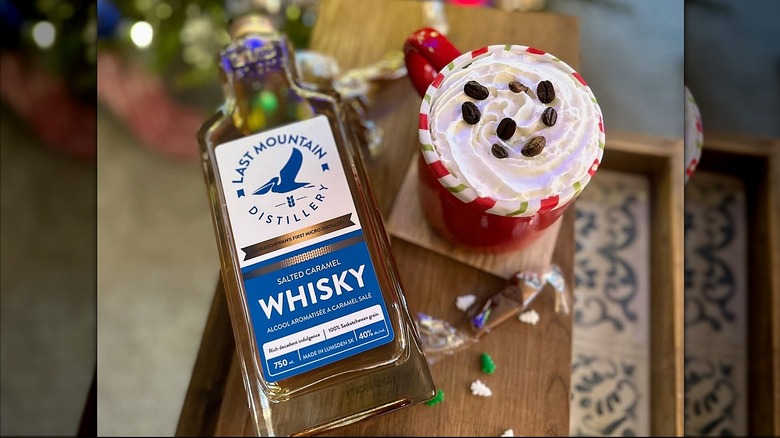 Bottle of Last Mountain Distillery Salted Caramel Whisky next to a festive mug with whipped cream and coffee beans.