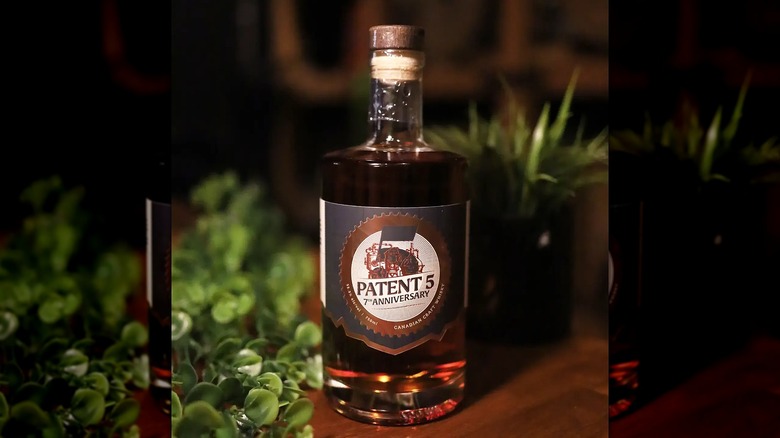 Bottle of Patent 5 Whisky on table surrounded by greenery.
