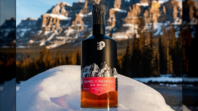 Bottle of Wild Life King of the North Whisky in snow pile, mountains in background.