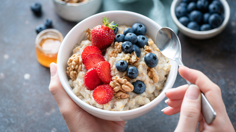 Hands holding spoon and bowl of oatmeal topped with berries