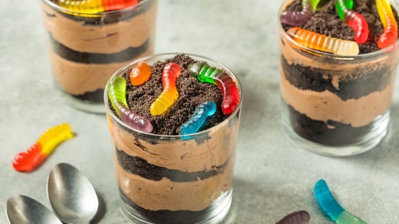 Individual glasses of dirt cake with gummy worms on top and spoons