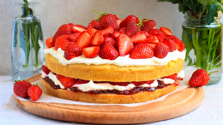 Strawberry shortcake topped with fresh strawberries and whipped cream on a serving board beside flower vases