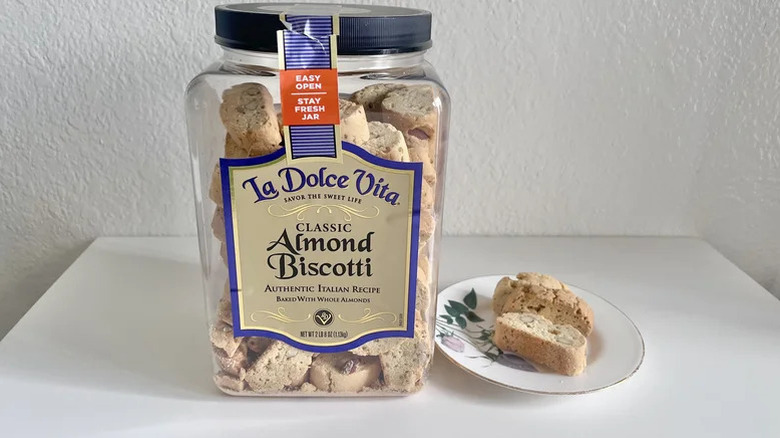 Container of La Dolce Vita Biscotti on a table with two cookies on a plate next to it
