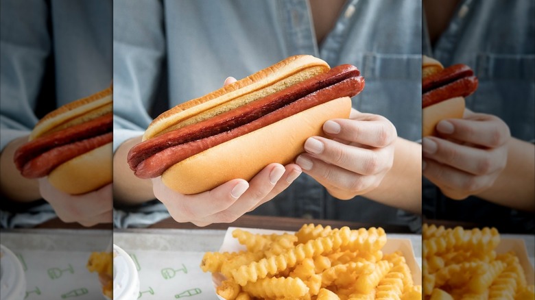 Customer holding Shake Shack Hot Dog with both hands above box of crinkle cut fries