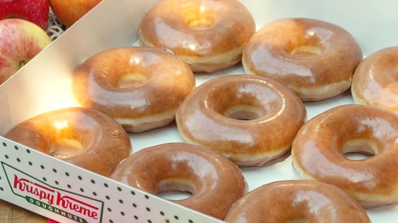 Rows of Krispy Kreme Apple Cider Glazed Donuts inside white box with apples besides