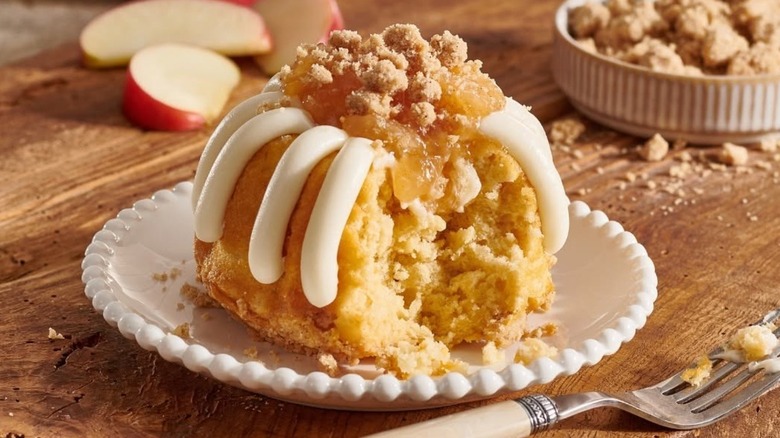 Nothing Bundt Cakes Apple Pie Cake on white plate on top of wooden board with fork plus apples in background