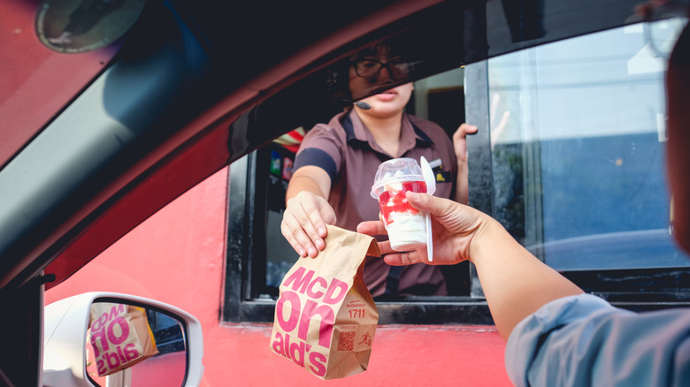 A McDonald's worker serving someone in their car at the drive-thru
