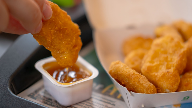 Hand dipping McDonald's nugget in sauce next to an open box of nuggets