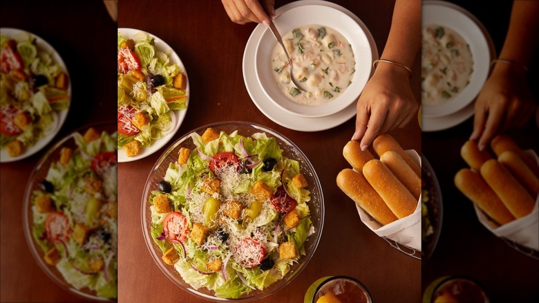 top view of Olive Garden table with salad, soup, and hand reaching for breadsticks, mirrored border