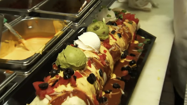 giant burrito being prepared next to metal containers of ingredients
