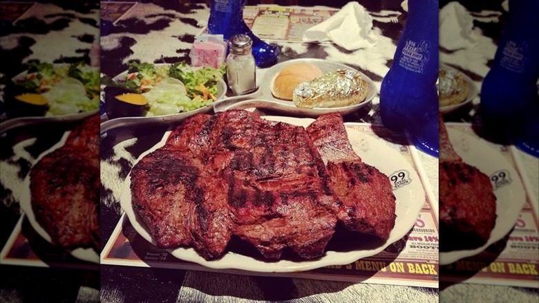 The 72-ounce Texan steak on a white plate with sides on calf skin table