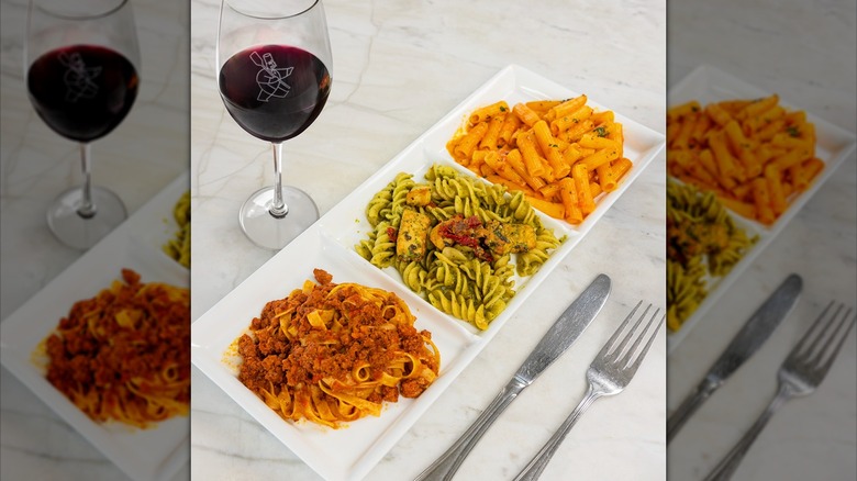 a platter of three different pastas and a glass of wine