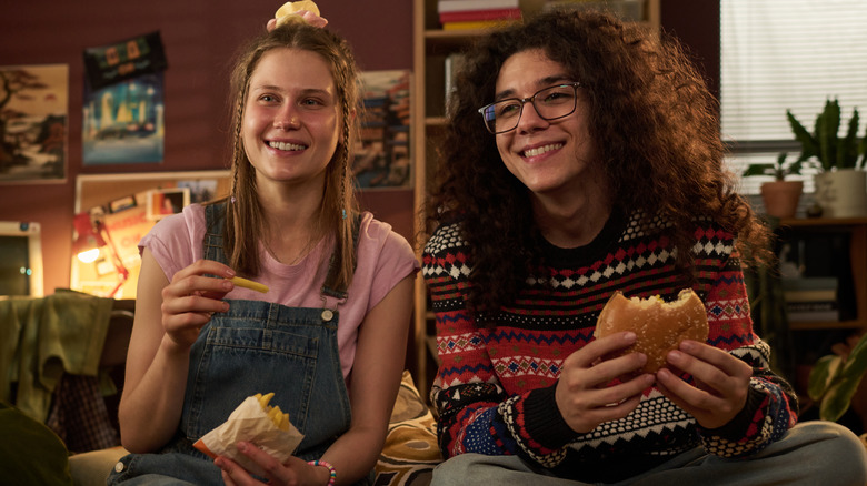 Two friends eating burgers and fries at home