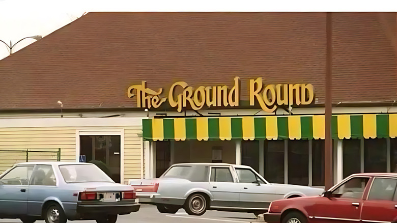 The facade of an outlet for The Ground Round, with a few cars in the parking lot.