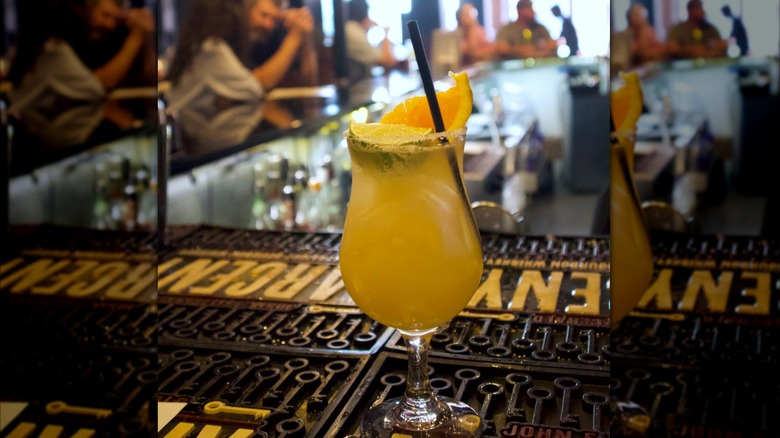 The Melting Pot's Freshly Picked Margarita topped with orange and lime on a bartop, with blurred diners at the bar in the background, with mirror borders