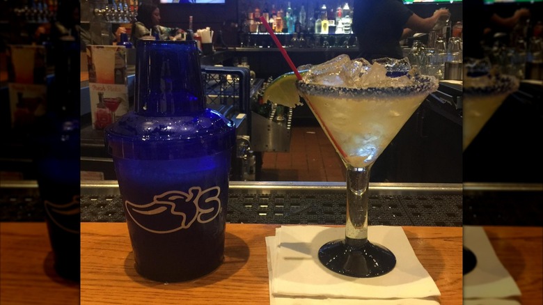 Chili's Presidente Margarita beside a blue shaker on a bartop facing the bar, with mirror borders