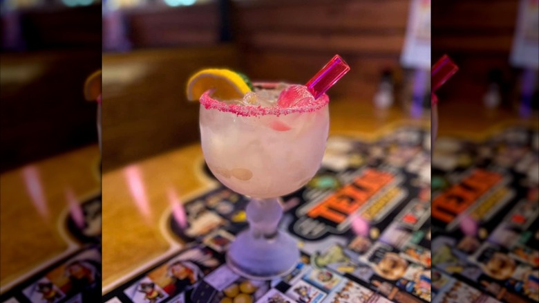 Texas Roadhouse's Legend Margarita on a table with a blurred background, with a pink salt rim and lemon garnish, with mirror borders