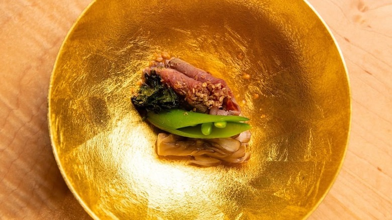elegantly plated meat and vegetables on a gold plate from Hiden, Miami