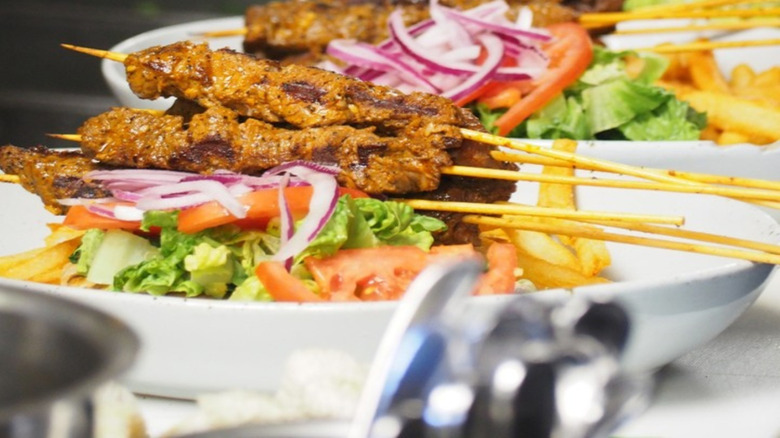 meat skewers plated over salad at Mandolin Aegean Bistro in Miami