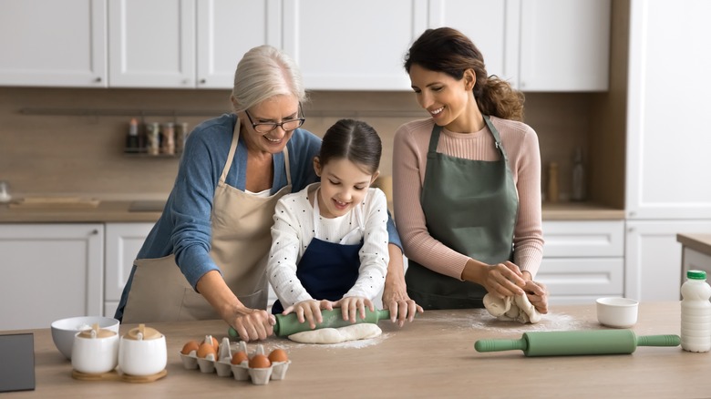 Three generations rolling out dough together in the kitchen