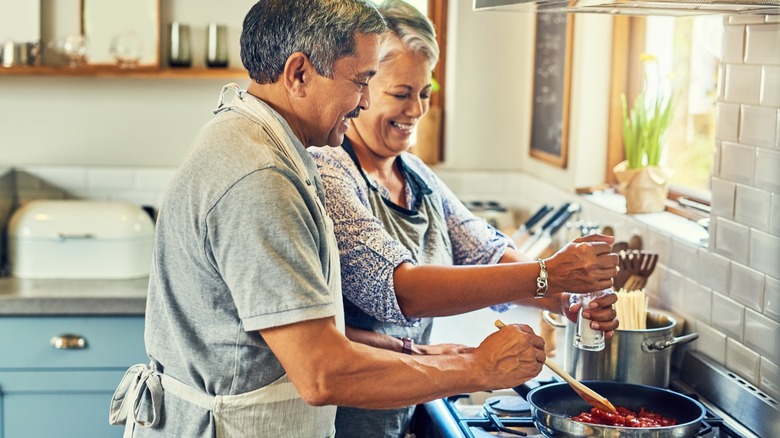 A grey-haired couple cooking together in the kitchen