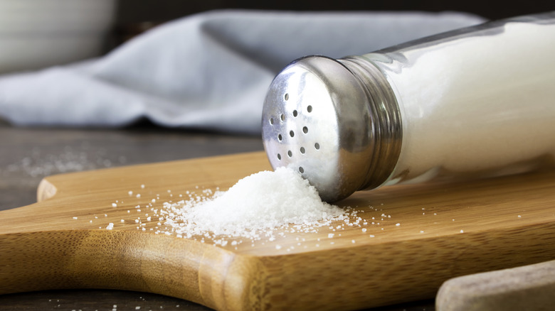 Salt shaker spilling salt onto a wooden cutting board